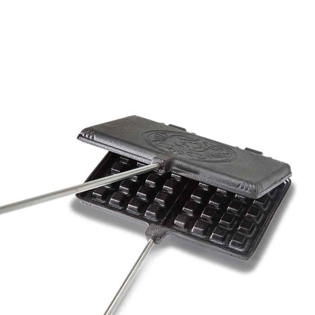 Gietijzeren Petromax wafelijzer met lange stelen, houten handgrepen en een wafelpatroon voor het bakken van verse wafels boven open vuur.