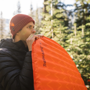 Persoon blaast de rode Therm-a-Rest ProLite Apex Heat Wave L slaapmat op in een bergachtige omgeving