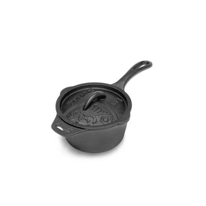Een zwarte gietijzeren Petromax sauspan met deksel die te midden van gloeiende kolen staat tijdens een outdoor kookbijeenkomst.