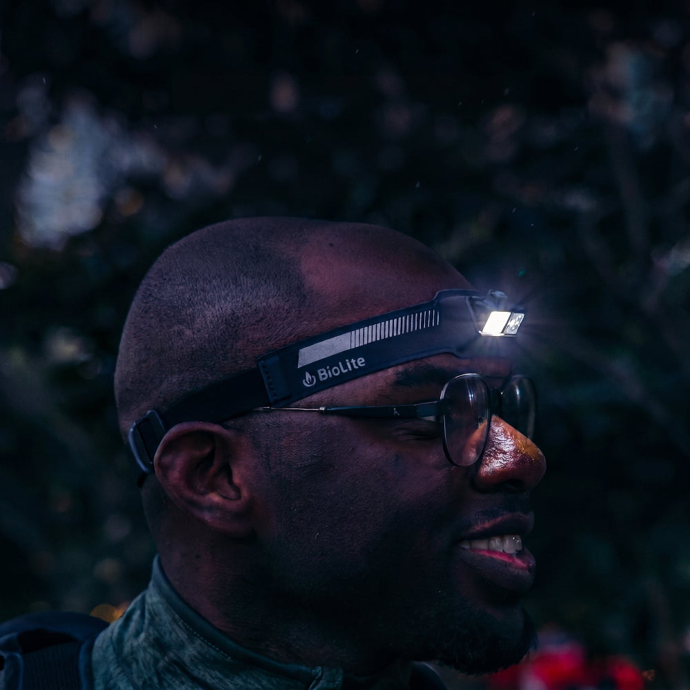 Zijkant profiel van een man die de zwarte BioLite HeadLamp 440 draagt, de lamp is aan en werpt licht opzij, duidelijke pasvorm.