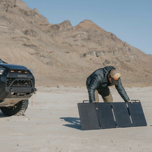 BioLite SolarPanel 100 opvouwbaar draagbaar zonnepaneel dat wordt opgesteld naast een terreinwagen in een woestijnlandschap