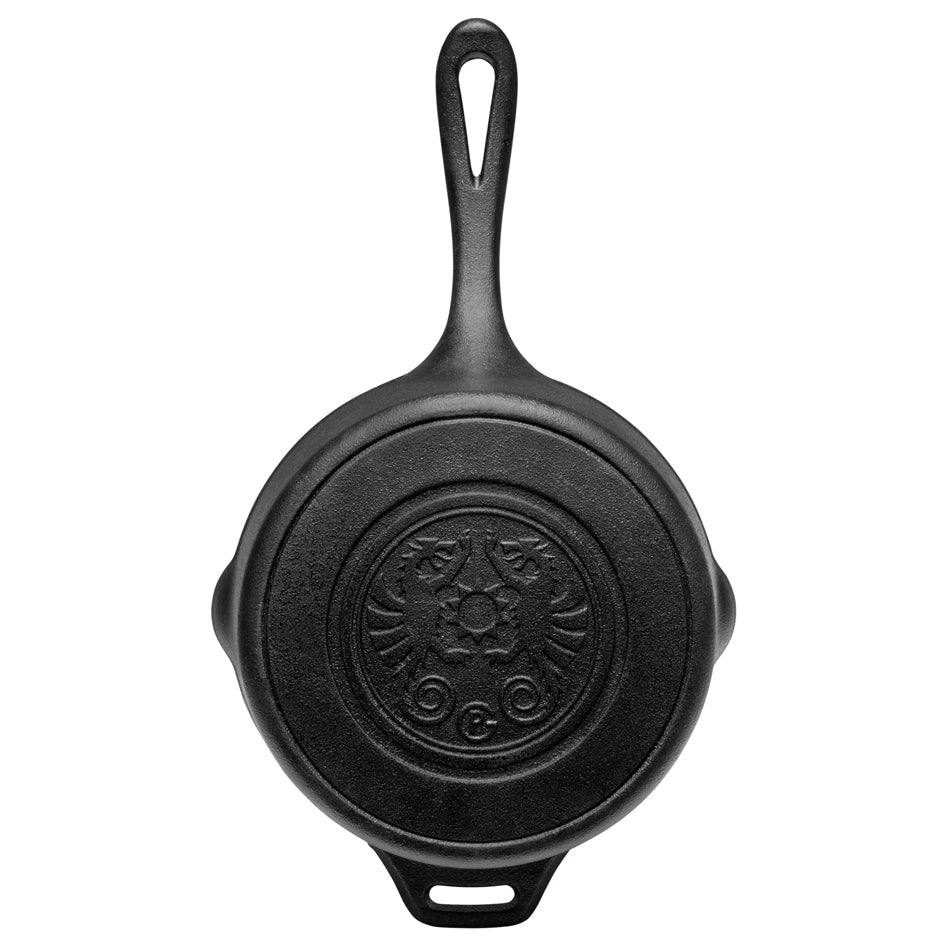 Een zwarte gietijzeren Petromax sauspan met deksel die te midden van gloeiende kolen staat tijdens een outdoor kookbijeenkomst.