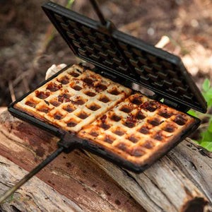 Gietijzeren Petromax wafelijzer met lange stelen, houten handgrepen en een wafelpatroon voor het bakken van verse wafels boven open vuur.