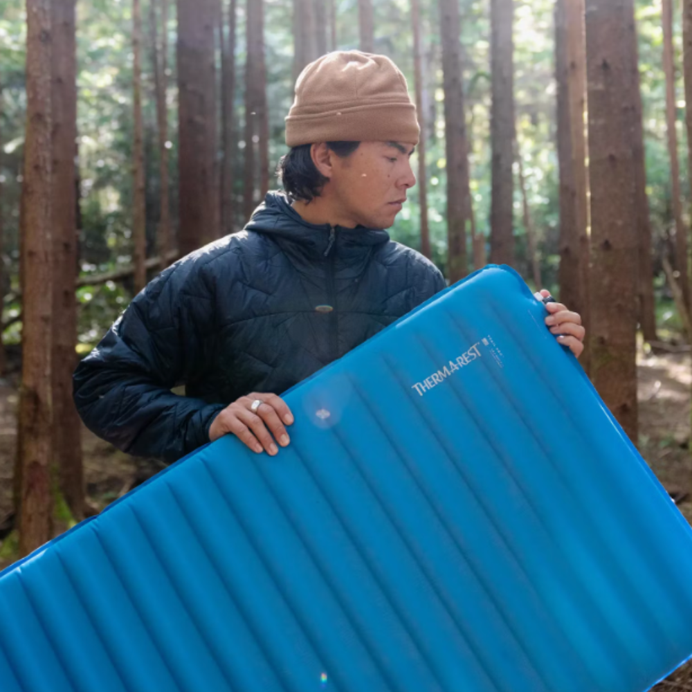 Therm-a-Rest Trail Pro MAX slaapmat vastgehouden door een persoon in een bosrijke omgeving