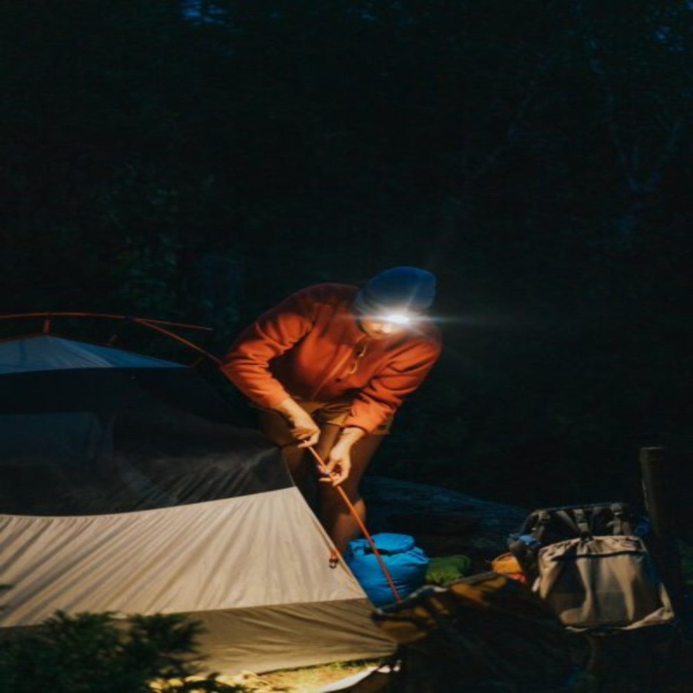 oplaadbare LED hoofdlamp die fel licht schijnt terwijl een kampeerder in het donker een tent opzet
